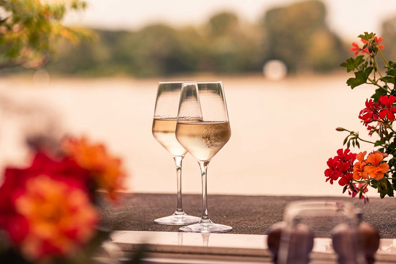 Zwei Gläser Weißwein vor dem Rhein im Sommerlicht